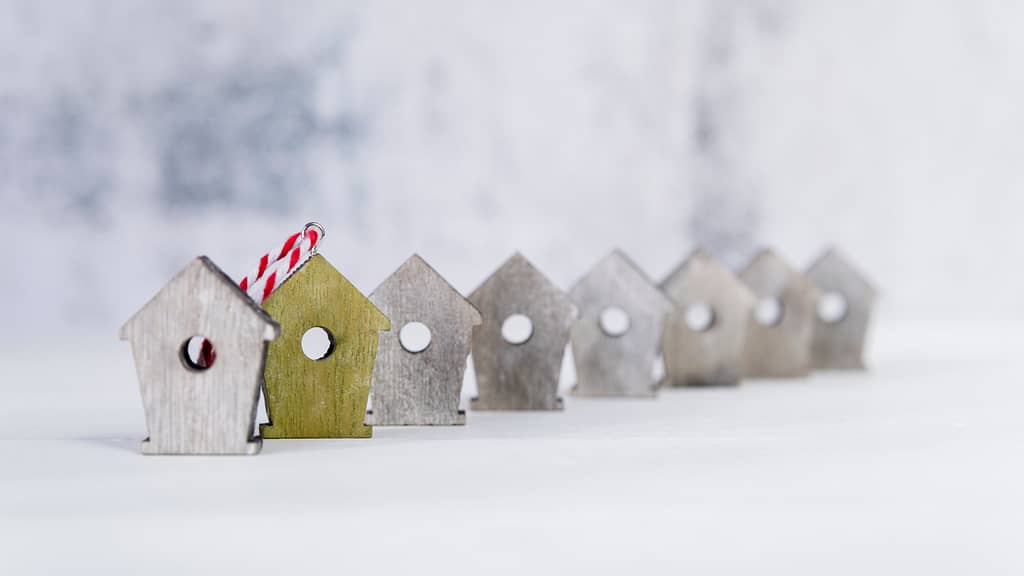 Row of small wooden house ornaments with one painted in gold, symbolizing real estate investment