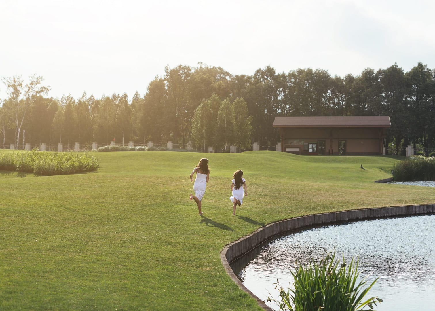 Two young girls running across a green lawn by a pond at a luxury Sotogrande estate