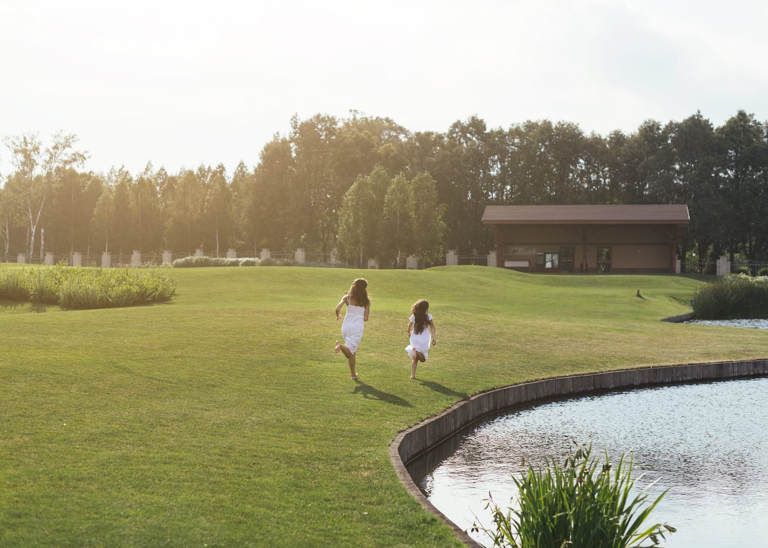 Two young girls running across a green lawn by a pond at a luxury Sotogrande estate