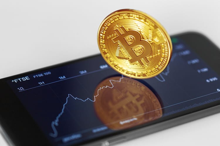 Gold Bitcoin coin on a smartphone displaying a stock market chart