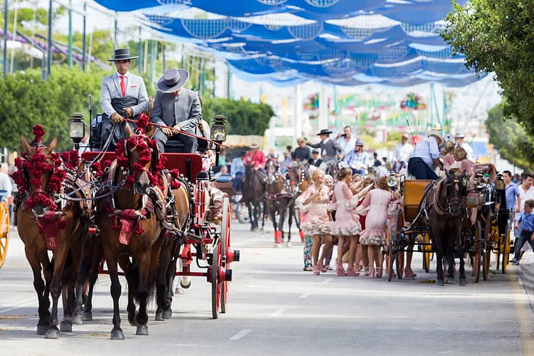Traditional horse-drawn carriages and people dressed in Spanish attire during a cultural festival in Sotogrande, Spain