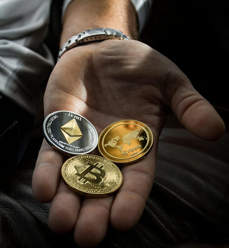 Hand holding cryptocurrency coins including Bitcoin, Ethereum, and Ripple.