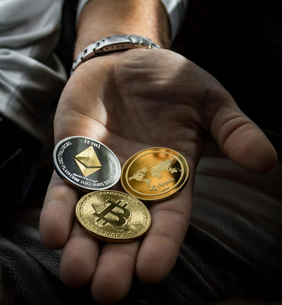Hand holding cryptocurrency coins including Bitcoin, Ethereum, and Ripple.